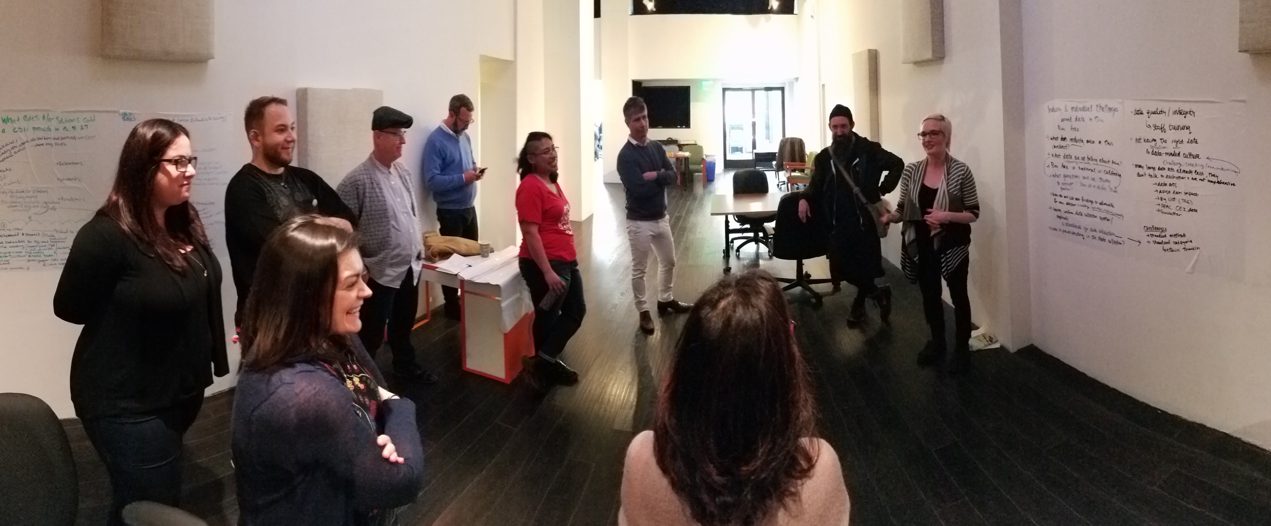 Photo of a BACDN meeting with several people standing in a circle discussing information on a white board