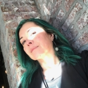 Portrait of Midori (dappled light on their face, wavy green hair, leaning against a brick wall)