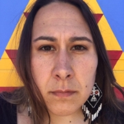 Close-up portrait, long straight brown hair and brown eyes, looking into the camera, one beaded earring showing, patterned background