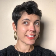 Portrait looking up and to the side, short brown hair, gold hoop earrings, black short