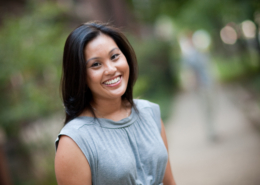 Dominique Enriquez smiling in a gray blouse against a blured background of greenery