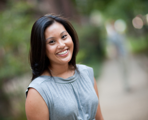 Dominique Enriquez smiling in a gray blouse against a blured background of greenery