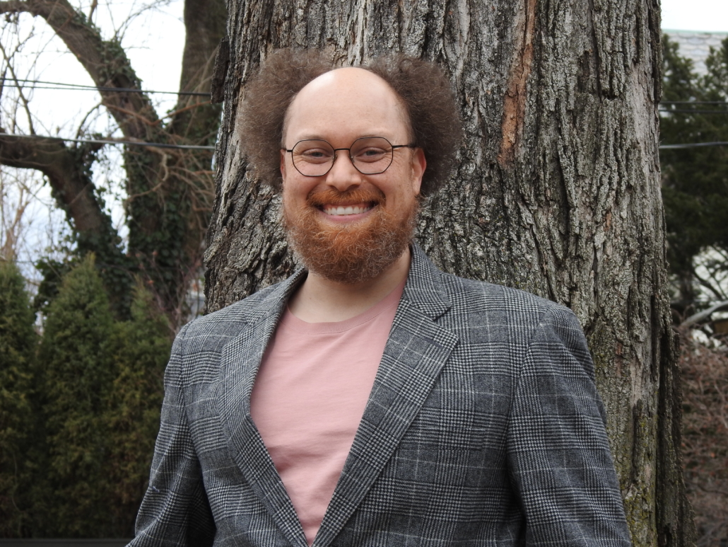 Stephan McLeroy in a gray sportscoat and salmon T-shirt in front of a large tree and greenery