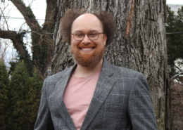 Stephan McLeroy in a gray sportscoat and salmon T-shirt in front of a large tree and greenery