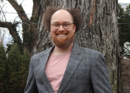 Stephan McLeroy in a gray sportscoat and salmon T-shirt in front of a large tree and greenery