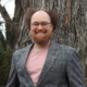 Stephan McLeroy in a gray sportscoat and salmon T-shirt in front of a large tree and greenery