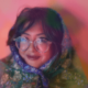 Sharmi Basu wrapped in a colorful scarf wearing wide circle glasses against a pink background